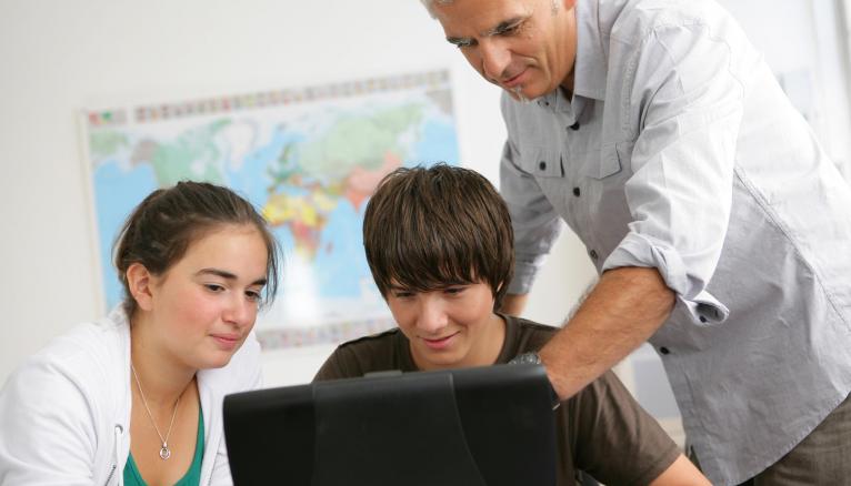 Portrait d'un jeune garçon et d'une fille devant un ordinateur portable en salle de cours près d'un homme