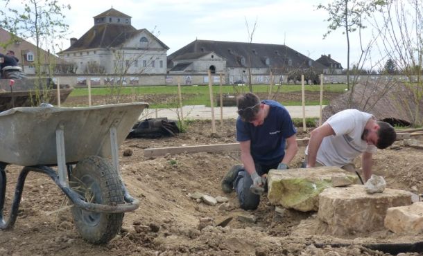 Thomas et Thomas agencent les pierres qui serviront de marches dans une future mare, avec, au loin, le bâtiment de la Saline Royale.
